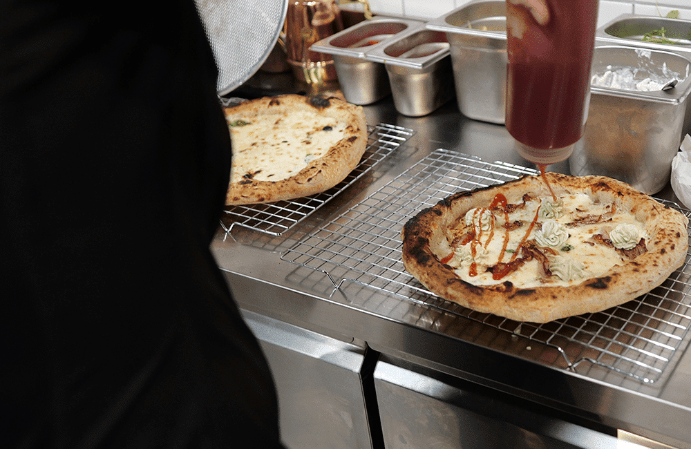 Fotografía del pizzaiolo echando una salsa por encima de una de las pizzas de Gussa pizzería en Gandia | Obrador Napolitano | Para llevar | To take away | Pizza Napolitana